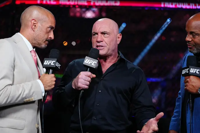 Tre menn holder UFC-mikrofoner i en samtale på en arena. Den sentrale mannen gestikulerer mens han snakker
