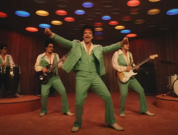 Bandet opptrer energisk på scenen i retro-stil antrekk og bakteppe, med ett medlem som synger foran og andre spiller instrumenter