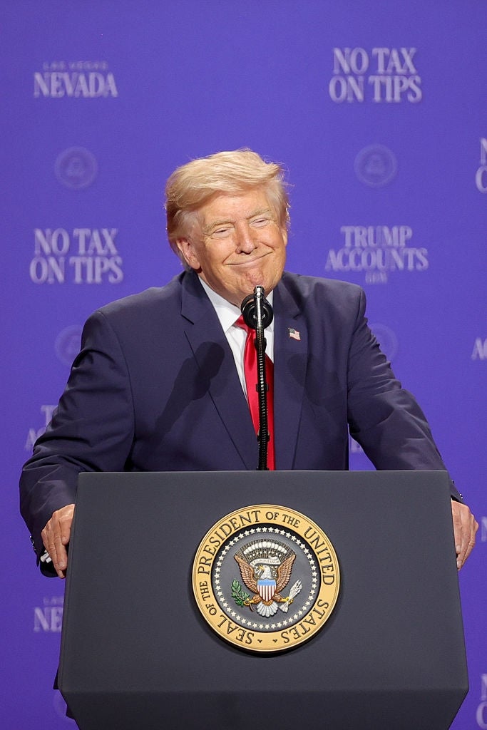 En person i dress smiler mens han snakker på et podium med presidentforseglingen, foran et bakteppe med «Ingen skatt på tips»; og "Trump Accounts Inc."