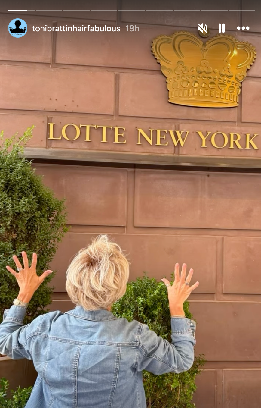 Person med kort hår i dongerijakke poserer med ryggen mot kameraet og gestikulerer begeistret foran Lotte New York Palace-skiltet
