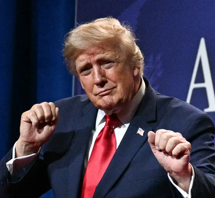 En mann i dress på scenen gestikulerer med nevene hevet. En bakgrunn viser setninger som "Powering American" og "Ingen skatt på tips."