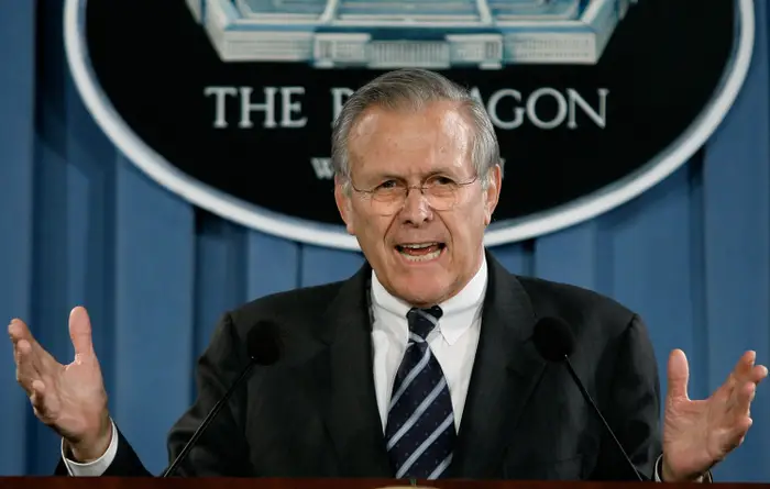 En person i dress og slips snakker ettertrykkelig ved et podium med «The Pentagon»; vises bak dem