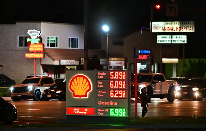 Folk som går forbi en Shell bensinstasjon om natten; skiltet viser høye bensinpriser fra $5,89 til $6,99