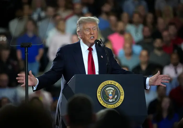 En mann i dress gestikulerer mens han snakker ved et podium merket «President of the United States»; foran en folkemengde