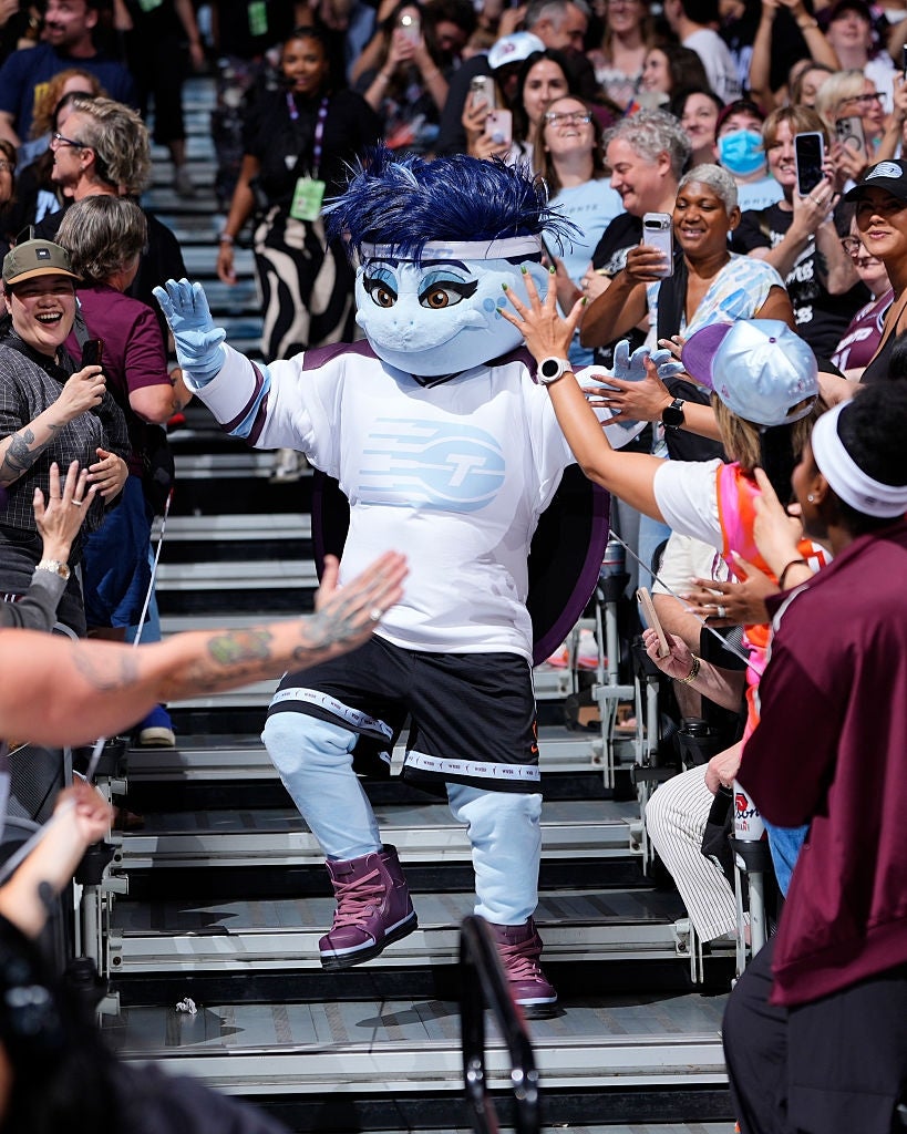 Maskot i sportsantrekk high-fives heier publikum på stadiontribunen