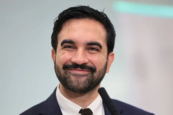 Zohran Mamdani, i profesjonelt antrekk, smiler på en talebegivenhet,