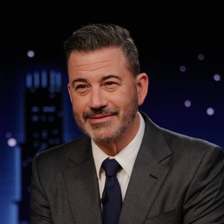 En person i dress sitter ved et skrivebord med et navneskilt som leser «Jimmy Kimmel», i et talkshow-miljø sent på kvelden