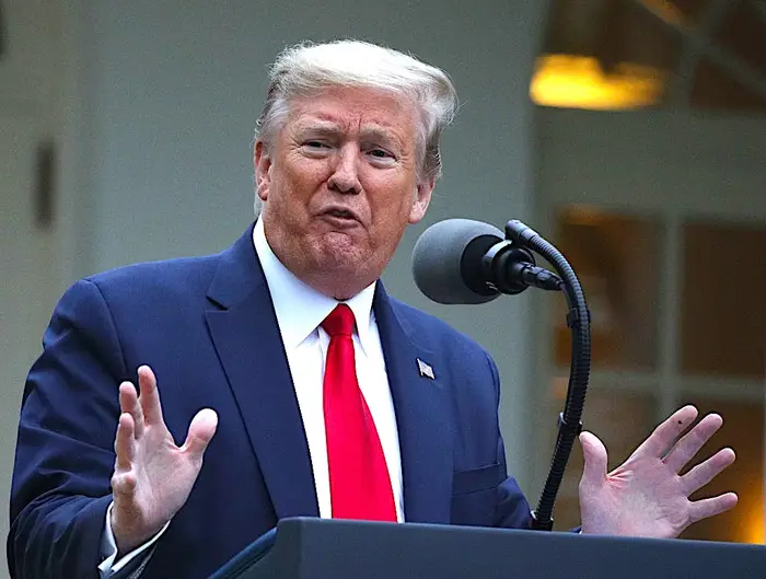 Donald Trump, i dress og slips, taler ved et podium med mikrofon i en utendørs setting