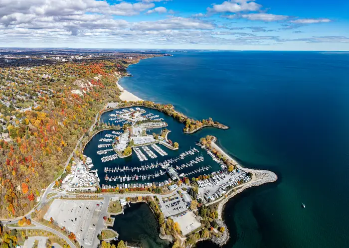 Luftfoto av en marina med parkerte båter, omgitt av naturskjønn kystlinje og høstløvverk