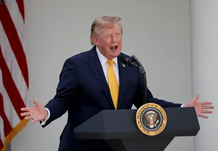 En person snakker lidenskapelig ved et podium med en presidentsegl, utendørs, ved siden av et amerikansk flagg