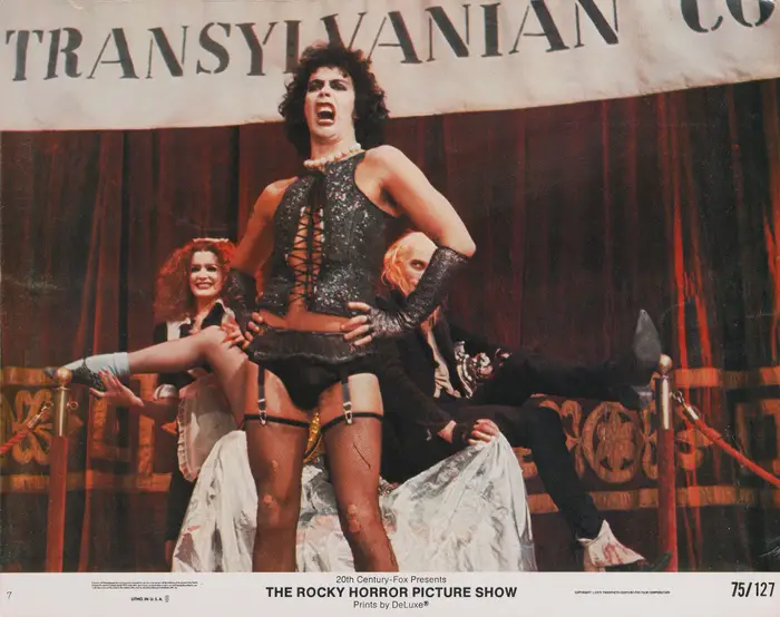 Tre skuespillere opptrer på scenen i teatralske kostymer for «The Rocky Horror Picture Show," med én karakter i korsett og nettstrømper