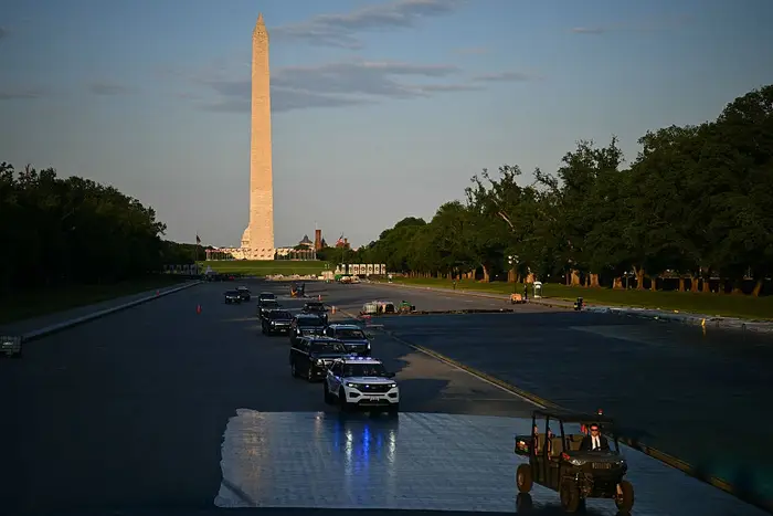 Rekke med kjøretøy med lys på nær Washington-monumentet, med en fjern, fredelig parkomgivelse