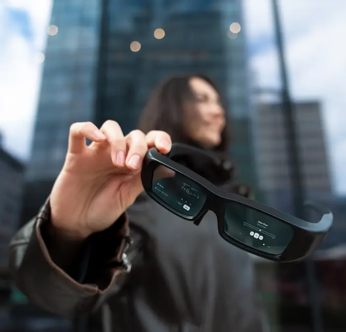 En person som holder smarte briller med digitale skjermer foran en uskarp urban bakgrunn