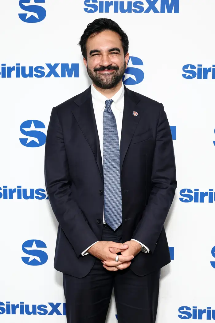 En person i dress og slips smiler på bakgrunn av et SiriusXM-arrangement
