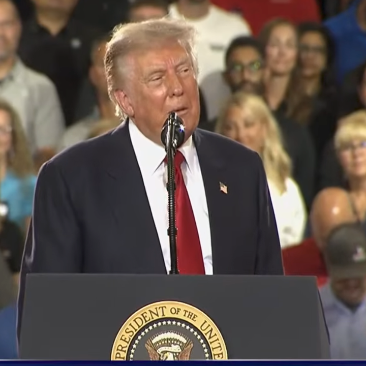 En person taler ved et podium med et presidentstempel og henvender seg til et publikum på et arrangement