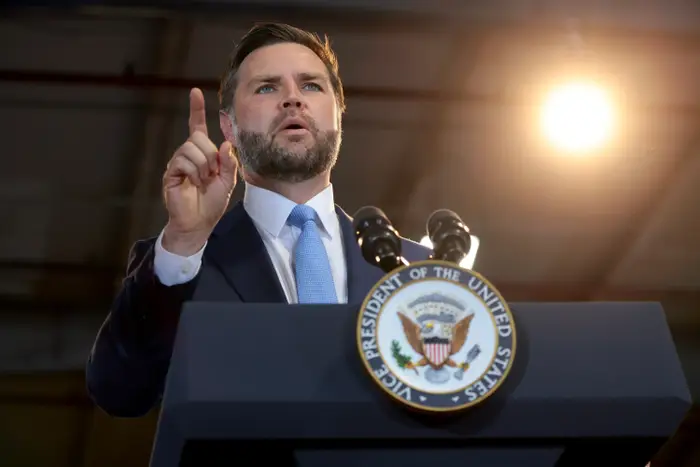 En mann i dress gestikulerer mens han snakker på et podium med visepresidenten i USA