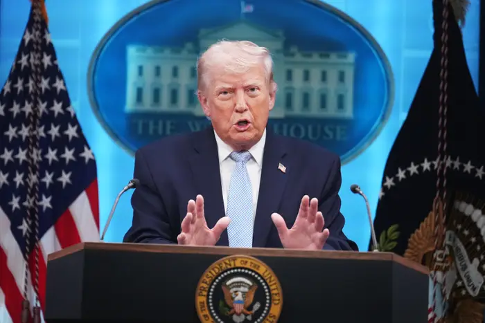 En person i dress taler ved et podium med presidentseglet, flankert av amerikanske flagg og Det hvite hus-emblemet i bakgrunnen