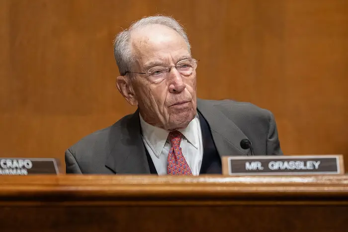 Chuck Grassley sitter, iført dress og slips, i formelle omgivelser med navneskiltet synlig foran