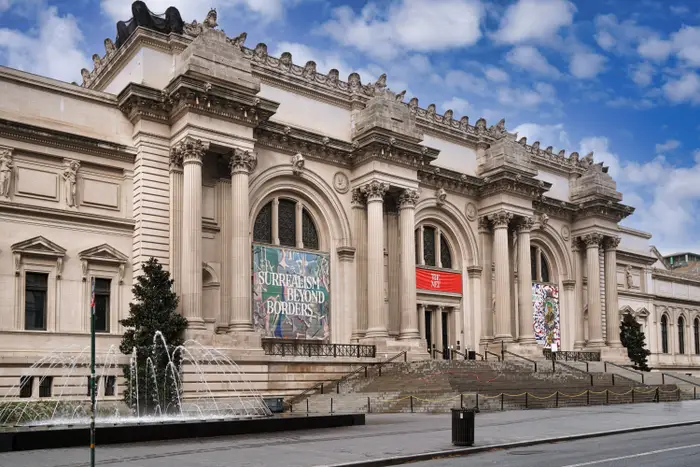 Fasaden til Metropolitan Museum of Art med bannere som viser utstillingstitler, satt mot en klar himmel