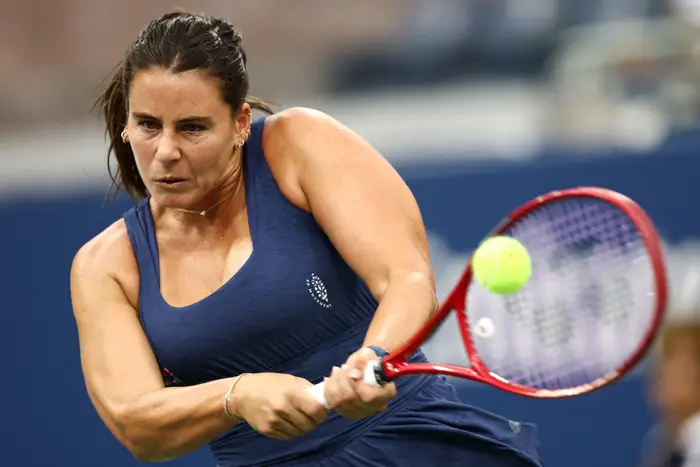 Person som spiller tennis, med fokus på å slå et bakhåndsskudd med en rød racket