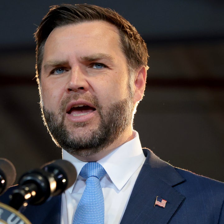 Person i dress som snakker ved et podium med segl, gjør en gest med løftet hånd, formidler en formell adresse eller tale