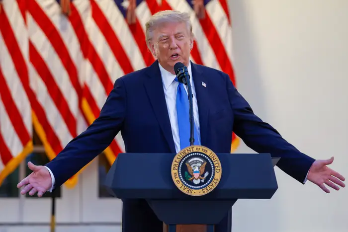 En person i dress snakker ved et podium med flere amerikanske flagg i bakgrunnen