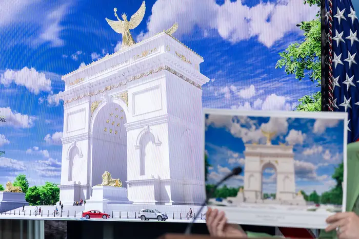 En person holder et illustrert bilde av et klassisk buemonument foran en stor skjerm som viser en lignende arkitektonisk design