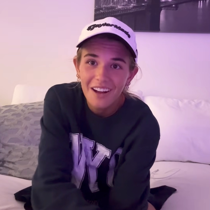 Person som har på seg en New York-genser og en caps, sitter på en sofa i uformelle omgivelser