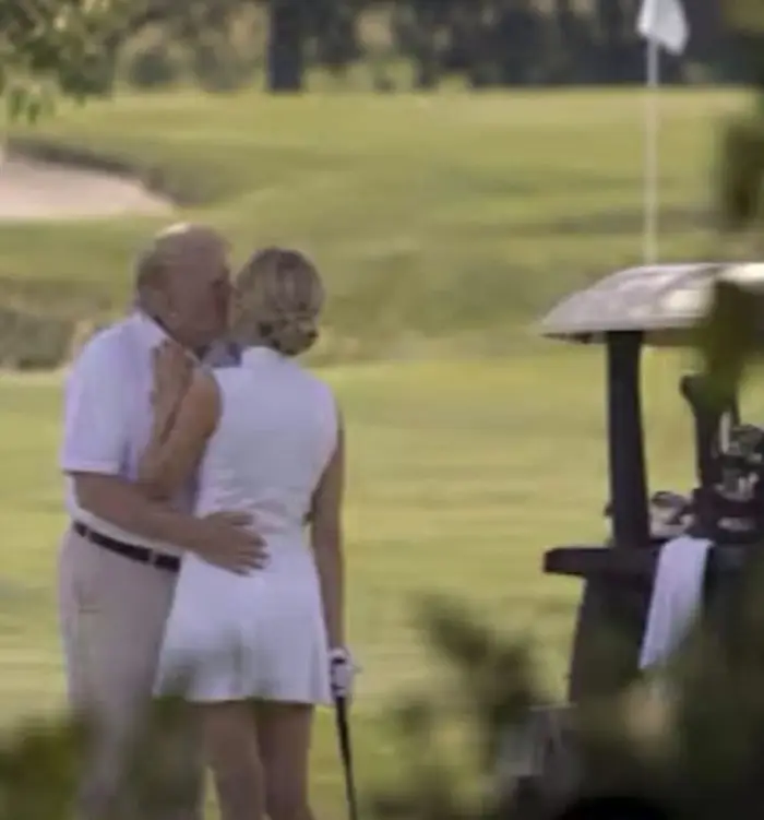 Et par på en golfbane deler et kyss i nærheten av en golfbil, med et flagg synlig i det fjerne