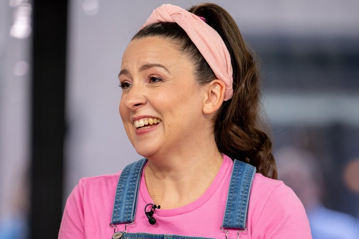 Person som smiler, iført dongeridress og en rosa skjorte med pannebånd, i uformelle omgivelser
