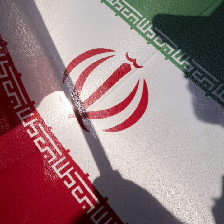 Skygge av en person som holder en flaggstang, støpt på det iranske flagget, med det sentrale emblemet og dekorative mønstre