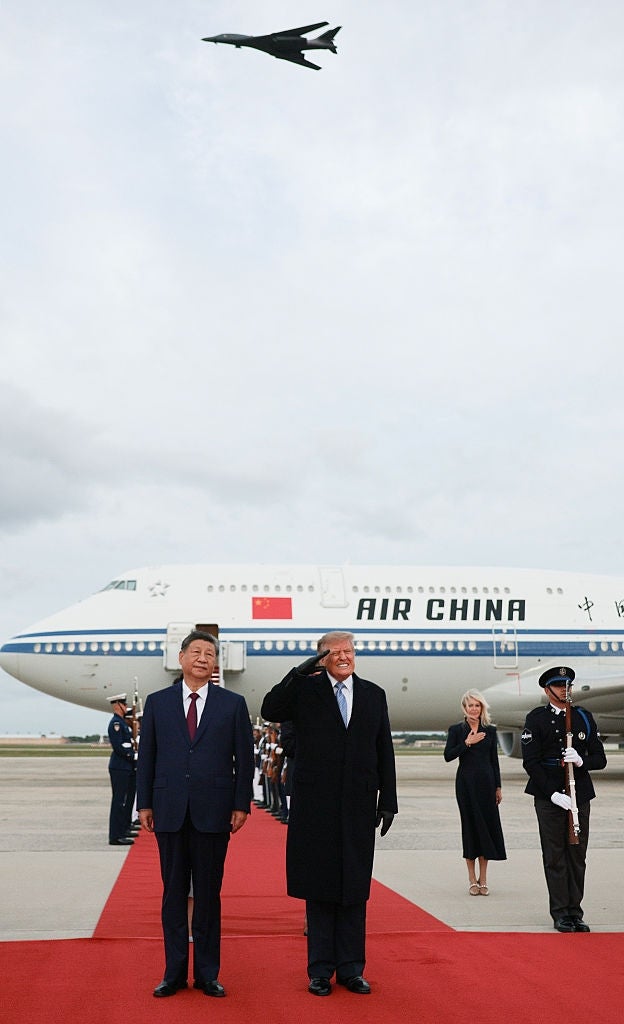 To ledere står på en rød løper foran et Air China-fly, mens et fly flyr over hodet. De er kledd i formell antrekk