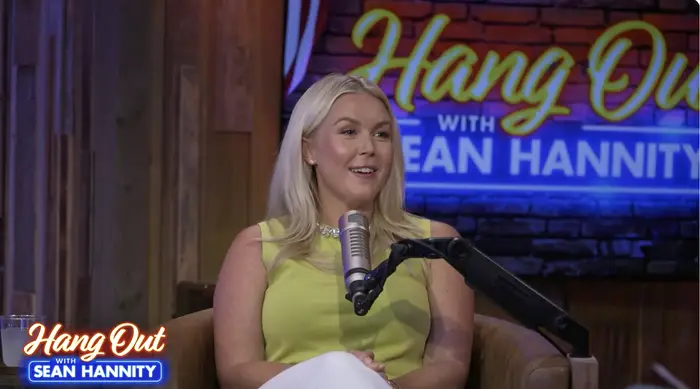 Person som snakker inn i en mikrofon under en "Heng Out with Sean Hannity" show, iført en ermeløs topp. Bakgrunnen viser showlogoen