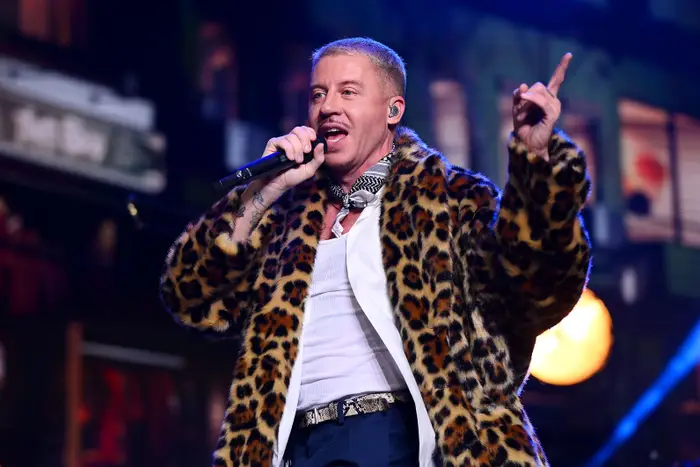 Person som opptrer på scenen i en frakk med leopardmønster, synger inn i en mikrofon med et animert uttrykk