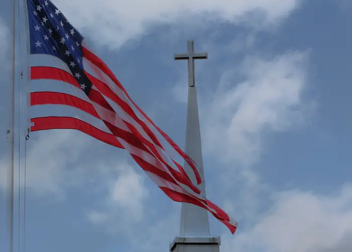 Amerikansk flagg bølger nær et kirketårn toppet med et kors mot en delvis overskyet himmel