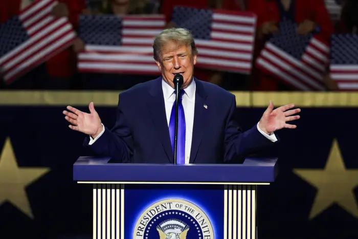 En person i dress snakker på et podium med et presidentsegl, holder hendene ut, med amerikanske flagg i bakgrunnen