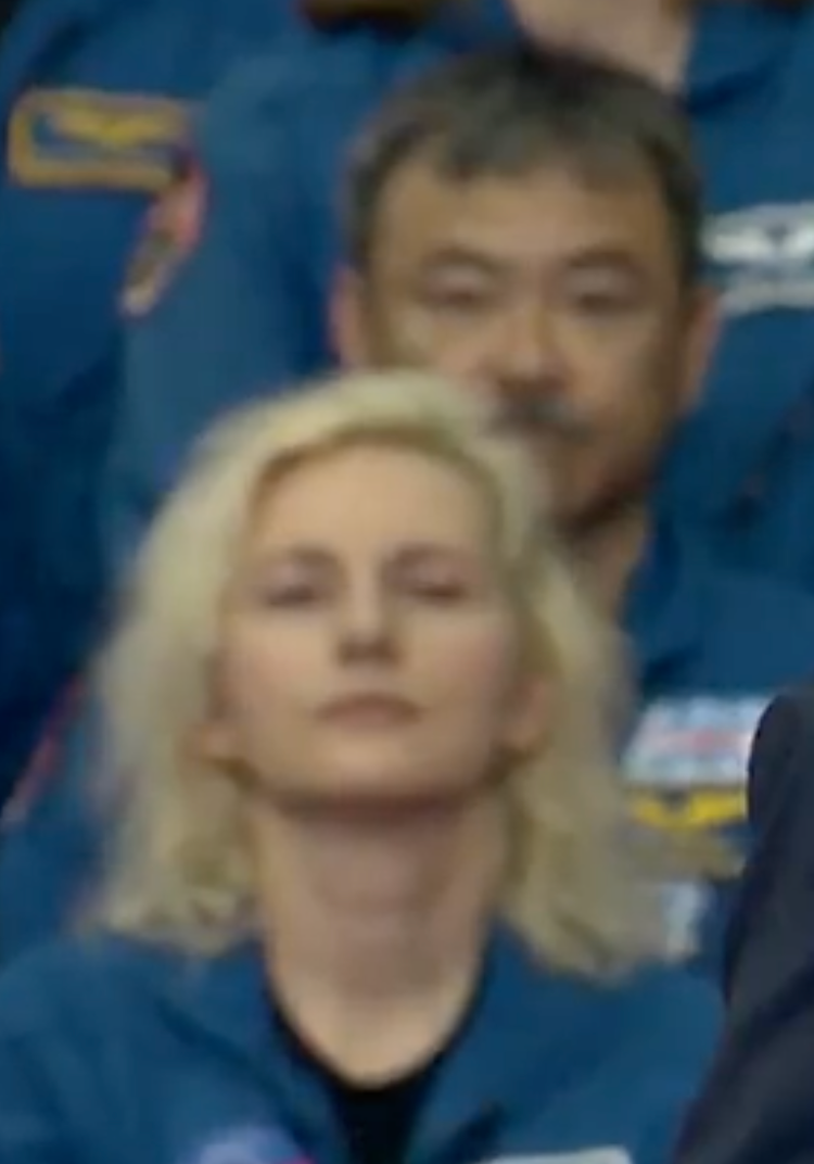 En gruppe mennesker i uniformer, muligens astronauter, med én person i forgrunnen. Uttrykkene deres er nøytrale
