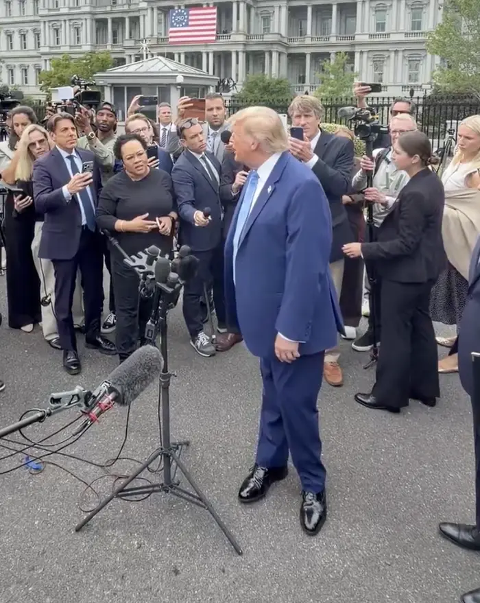 En person i dress snakker med journalister utenfor en bygning mens flere mikrofoner peker mot dem