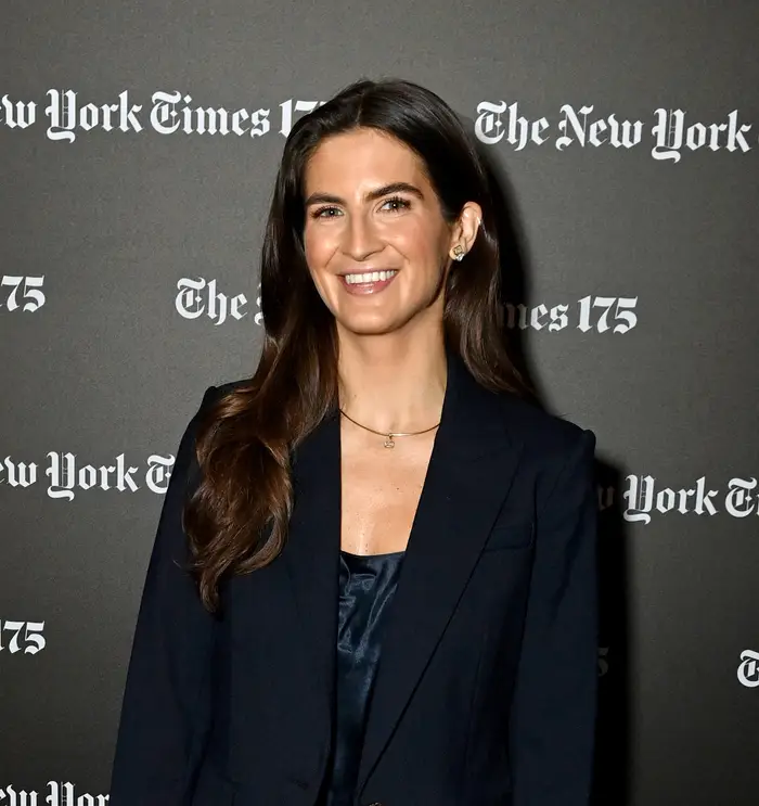Person på arrangementsteppe iført mørk blazer og brede jeans, smiler og holder en telefon. Bakteppet inneholder "The New York Times 175" tekst