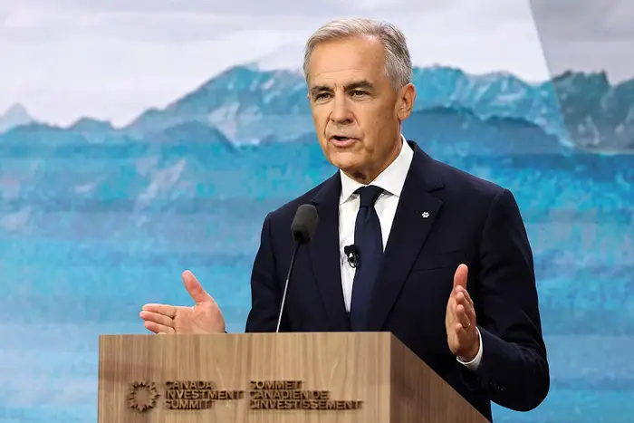 En mann i dress taler selvsikkert ved et podium under Canada Investment Summit. Fjell er synlige i bakgrunnen
