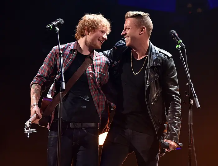 Ed Sheeran og Macklemore smiler med armene rundt hverandre på scenen
