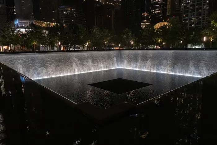 Opplyst 9/11 minnefontene med brusende vann, omgitt av trær og bylys om natten