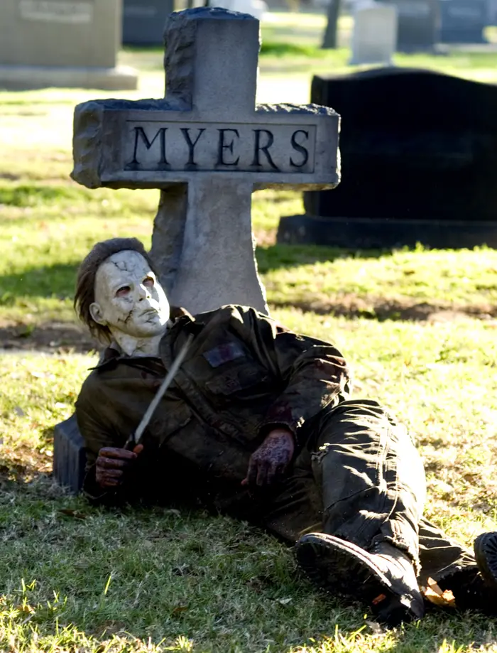 Michael Myers iført maske og jumpsuit ligger ved siden av en gravstein merket