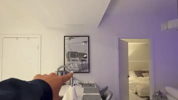 En person peker på et innrammet bilde på en vegg i en moderne, minimalistisk leilighet med en åpen soveromsdør i bakgrunnen