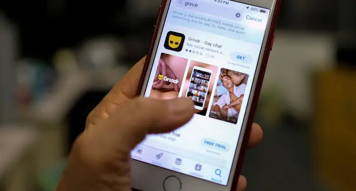 En hånd som holder en telefon som viser Grindr-appens side i en digital butikk, og fremhever tilgjengeligheten for nedlasting