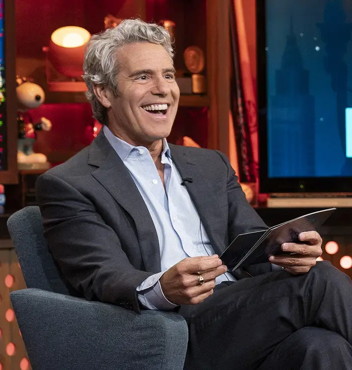 To personer sitter smilende på et talkshowsett med et skilt der det står 