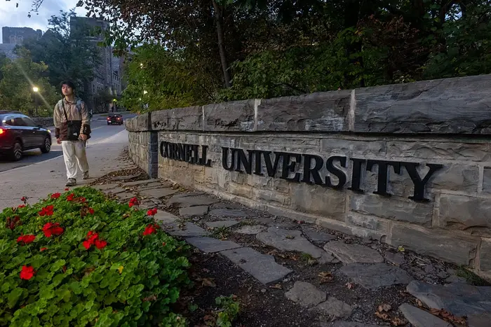 Person som går på campus ved Cornell University, omgitt av trær og et blomsterbed