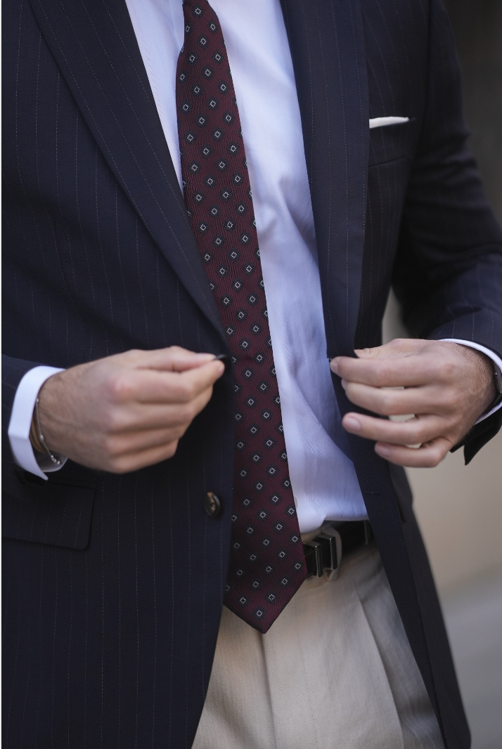 Person som justerer en mørk pinstripe dressjakke, har på seg et mønstret slips og lys skjorte, med beige bukser